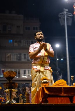 Varanasi, Uttar Pradesh, Hindistan - Kasım 2022: Ganga aarti, genç bir rahibin portresi Daswamedh ghat 'ta akşam üzeri sanatan hindu ayinleriyle geleneksel elbise içinde nehir çetelerini icra ediyor..