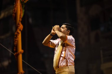 Varanasi, Uttar Pradesh, Hindistan - Kasım 2022: Ganga aarti, genç bir rahibin portresi Daswamedh ghat 'ta akşam üzeri sanatan hindu ayinleriyle geleneksel elbise içinde nehir çetelerini icra ediyor..