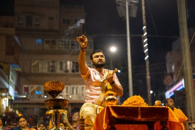 Varanasi, Uttar Pradesh, Hindistan - Kasım 2022: Ganga aarti, genç bir rahibin portresi Daswamedh ghat 'ta akşam üzeri sanatan hindu ayinleriyle geleneksel elbise içinde nehir çetelerini icra ediyor..