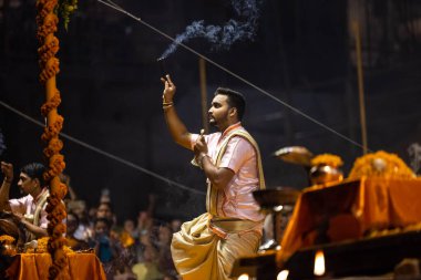 Varanasi, Uttar Pradesh, Hindistan - Kasım 2022: Ganga aarti, genç bir rahibin portresi Daswamedh ghat 'ta akşam üzeri sanatan hindu ayinleriyle geleneksel elbise içinde nehir çetelerini icra ediyor..