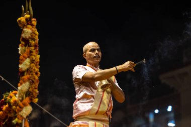 Varanasi, Uttar Pradesh, Hindistan - Kasım 2022: Ganga aarti, genç bir rahibin portresi Daswamedh ghat 'ta akşam üzeri sanatan hindu ayinleriyle geleneksel elbise içinde nehir çetelerini icra ediyor..