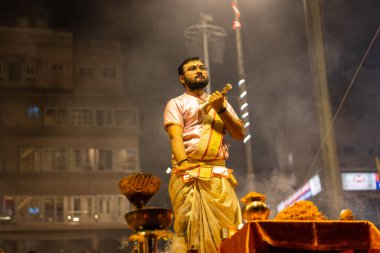 Varanasi, Uttar Pradesh, Hindistan - Kasım 2022: Ganga aarti, genç bir rahibin portresi Daswamedh ghat 'ta akşam üzeri sanatan hindu ayinleriyle geleneksel elbise içinde nehir çetelerini icra ediyor..