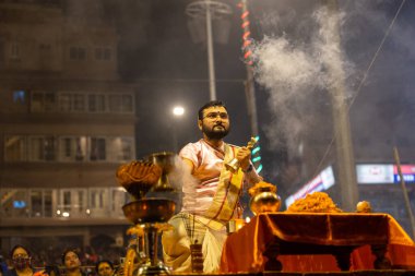 Varanasi, Uttar Pradesh, Hindistan - Kasım 2022: Ganga aarti, genç bir rahibin portresi Daswamedh ghat 'ta akşam üzeri sanatan hindu ayinleriyle geleneksel elbise içinde nehir çetelerini icra ediyor..