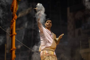 Varanasi, Uttar Pradesh, Hindistan - Kasım 2022: Ganga aarti, genç bir rahibin portresi Daswamedh ghat 'ta akşam üzeri sanatan hindu ayinleriyle geleneksel elbise içinde nehir çetelerini icra ediyor..