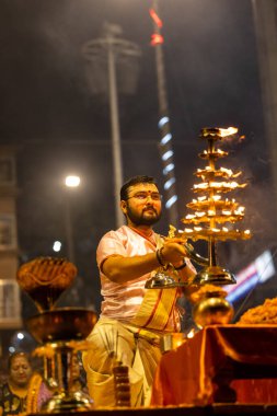 Varanasi, Uttar Pradesh, Hindistan - Kasım 2022: Ganga aarti, genç bir rahibin portresi Daswamedh ghat 'ta akşam üzeri sanatan hindu ayinleriyle geleneksel elbise içinde nehir çetelerini icra ediyor..