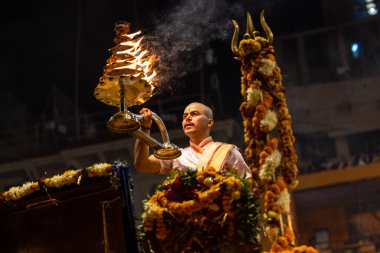 Varanasi, Uttar Pradesh, Hindistan - Kasım 2022: Ganga aarti, genç bir rahibin portresi Daswamedh ghat 'ta akşam üzeri sanatan hindu ayinleriyle geleneksel elbise içinde nehir çetelerini icra ediyor..