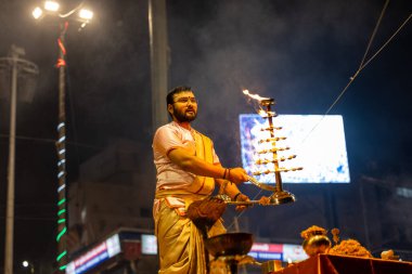 Varanasi, Uttar Pradesh, Hindistan - Kasım 2022: Ganga aarti, genç bir rahibin portresi Daswamedh ghat 'ta akşam üzeri sanatan hindu ayinleriyle geleneksel elbise içinde nehir çetelerini icra ediyor..