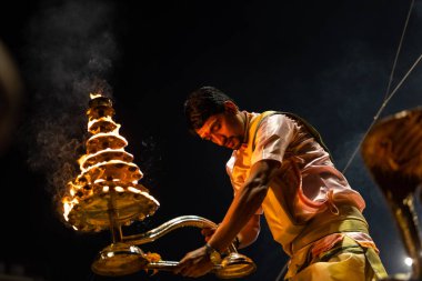 Varanasi, Uttar Pradesh, Hindistan - Kasım 2022: Ganga aarti, genç bir rahibin portresi Daswamedh ghat 'ta akşam üzeri sanatan hindu ayinleriyle geleneksel elbise içinde nehir çetelerini icra ediyor..