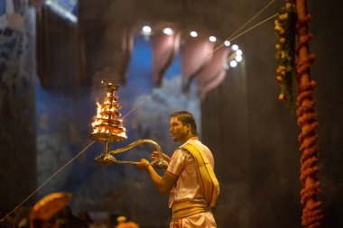 Varanasi, Uttar Pradesh, Hindistan - Kasım 2022: Ganga aarti, genç bir rahibin portresi Daswamedh ghat 'ta akşam üzeri sanatan hindu ayinleriyle geleneksel elbise içinde nehir çetelerini icra ediyor..