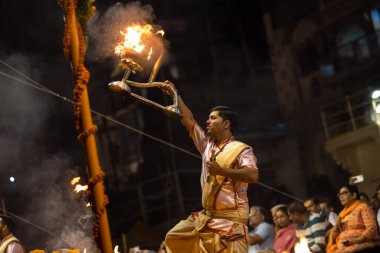 Varanasi, Uttar Pradesh, Hindistan - Kasım 2022: Ganga aarti, genç bir rahibin portresi Daswamedh ghat 'ta akşam üzeri sanatan hindu ayinleriyle geleneksel elbise içinde nehir çetelerini icra ediyor..