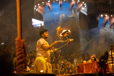 Varanasi, Uttar Pradesh, Hindistan - Kasım 2022: Ganga aarti, genç bir rahibin portresi Daswamedh ghat 'ta akşam üzeri sanatan hindu ayinleriyle geleneksel elbise içinde nehir çetelerini icra ediyor..
