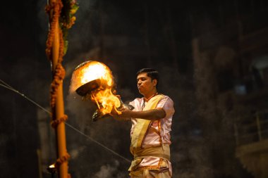 Varanasi, Uttar Pradesh, Hindistan - Kasım 2022: Ganga aarti, genç bir rahibin portresi Daswamedh ghat 'ta akşam üzeri sanatan hindu ayinleriyle geleneksel elbise içinde nehir çetelerini icra ediyor..