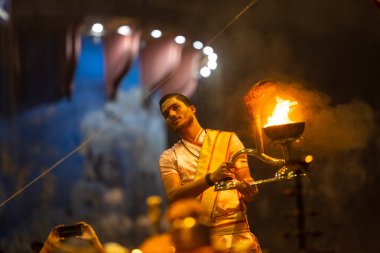 Varanasi, Uttar Pradesh, Hindistan - Kasım 2022: Ganga aarti, genç bir rahibin portresi Daswamedh ghat 'ta akşam üzeri sanatan hindu ayinleriyle geleneksel elbise içinde nehir çetelerini icra ediyor..