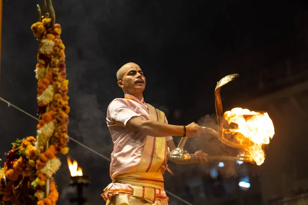 Varanasi, Uttar Pradesh, Hindistan - Kasım 2022: Ganga aarti, genç bir rahibin portresi Daswamedh ghat 'ta akşam üzeri sanatan hindu ayinleriyle geleneksel elbise içinde nehir çetelerini icra ediyor..