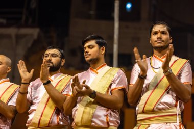 Varanasi, Uttar Pradesh, Hindistan - Kasım 2022: Ganga aarti, genç bir rahibin portresi Daswamedh ghat 'ta akşam üzeri sanatan hindu ayinleriyle geleneksel elbise içinde nehir çetelerini icra ediyor..