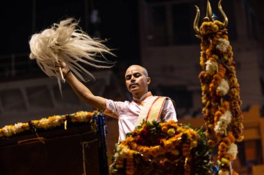 Varanasi, Uttar Pradesh, Hindistan - Kasım 2022: Ganga aarti, genç bir rahibin portresi Daswamedh ghat 'ta akşam üzeri sanatan hindu ayinleriyle geleneksel elbise içinde nehir çetelerini icra ediyor..
