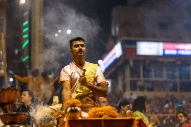 Varanasi, Uttar Pradesh, Hindistan - Kasım 2022: Ganga aarti, Dashashwamedh Ghat 'ta akşamüstü sanatan hindu ayinleriyle geleneksel elbise giymiş genç bir rahibin portresi.