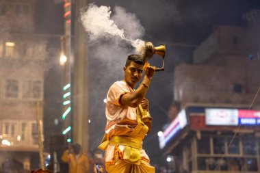 Varanasi, Uttar Pradesh, Hindistan - Kasım 2022: Ganga aarti, Dashashwamedh Ghat 'ta akşamüstü sanatan hindu ayinleriyle geleneksel elbise giymiş genç bir rahibin portresi.