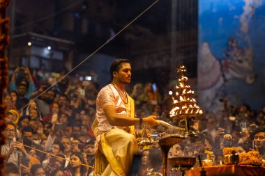 Varanasi, Uttar Pradesh, Hindistan - Kasım 2022: Ganga aarti, Dashashwamedh Ghat 'ta akşamüstü sanatan hindu ayinleriyle geleneksel elbise giymiş genç bir rahibin portresi.