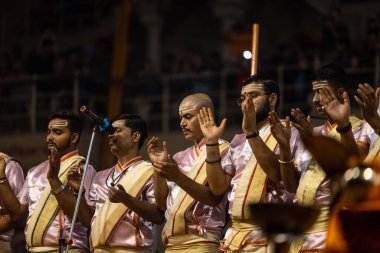 Varanasi, Uttar Pradesh, Hindistan - Kasım 2022: Ganga aarti, Dashashwamedh Ghat 'ta akşamları sanatan Hindu ayinleriyle geleneksel elbise içinde nehir çetelerini icra eden genç rahiplerin portresi.