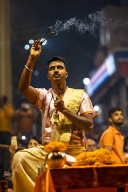 Varanasi, Uttar Pradesh, Hindistan - Kasım 2022: Ganga aarti, Dashashwamedh Ghat 'ta akşamüstü sanatan hindu ayinleriyle geleneksel elbise giymiş genç bir rahibin portresi.