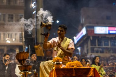 Varanasi, Uttar Pradesh, Hindistan - Kasım 2022: Ganga aarti, Dashashwamedh Ghat 'ta akşamüstü sanatan hindu ayinleriyle geleneksel elbise giymiş genç bir rahibin portresi.