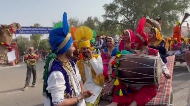 Bikaner, Rajasthan, Hindistan - Ocak 2023: Punjabi Bhangra, geleneksel Punjabi renkli elbise ve türban giymiş genç sih erkek grubu deve festivalinde gülümseyerek Punjabi bhangra dansı yapıyor.