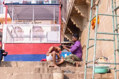 Varanasi, Uttar Pradesh, Hindistan - Kasım 2022: Sokak berberi, Varanasi 'deki Hindu ayinlerinin bir parçası olarak çetelerin yakınındaki Dashashwamedh Ghat' ta dindarların kafasını tıraş ediyor.