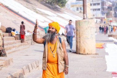 Varanasi, Uttar Pradesh, Hindistan - Kasım 2022: Geleneksel elbise içinde Varanasi şehrinde nehir çetelerinin yanındaki ghat üzerinde yürüyen tanımlanamayan Hint sadhu baba portresi. Varanasi en eski ve kutsal şehirdir..