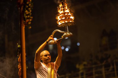 Varanasi, Uttar Pradesh, Hindistan - Kasım 2022: Ganga aarti, Dashashwamedh Ghat 'ta akşamüstü sanatan hindu ayinleriyle geleneksel elbise giymiş genç bir rahibin portresi.