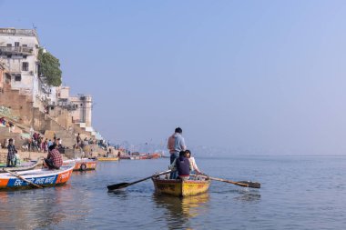 Varanasi, Uttar Pradesh, Hindistan - Kasım 2022: Turistler sabah erken saatlerde Varanasi 'deki martı sürüsüyle birlikte nehir çetelerinde tekne gezintisi yapıyorlar. Tahta teknede yelken açan kayıkçı.
