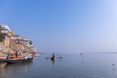 Varanasi, Uttar Pradesh, Hindistan - Kasım 2022: Turistler sabah erken saatlerde Varanasi 'deki martı sürüsüyle birlikte nehir çetelerinde tekne gezintisi yapıyorlar. Tahta teknede yelken açan kayıkçı.