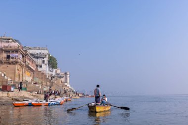 Varanasi, Uttar Pradesh, Hindistan - Kasım 2022: Turistler sabah erken saatlerde Varanasi 'deki martı sürüsüyle birlikte nehir çetelerinde tekne gezintisi yapıyorlar. Tahta teknede yelken açan kayıkçı.