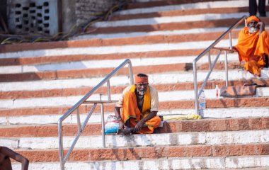 Varanasi, Uttar Pradesh, Hindistan - Kasım 2022: Kimliği belirsiz Hintli sadhu baba merdivenlerde oturuyor