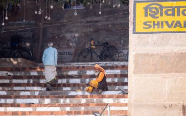 Varanasi, Uttar Pradesh, Hindistan - Kasım 2022: Kimliği belirsiz Hintli sadhu baba merdivenlerde oturuyor