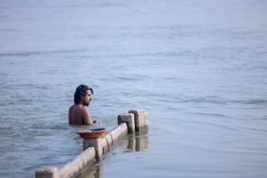Varanasi, Uttar Pradesh, Hindistan - Kasım 2022: Kimliği belirsiz erkek portresi Hindu ayinlerini gerçekleştirmek için gün doğumunda Ganj Nehri 'ne kutsal dalış yapıyor.