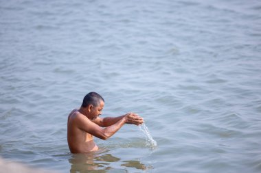 Varanasi, Uttar Pradesh, Hindistan - Kasım 2022: Kimliği belirsiz erkek portresi Hindu ayinlerini gerçekleştirmek için gün doğumunda Ganj Nehri 'ne kutsal dalış yapıyor.