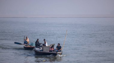 Varanasi, Uttar Pradesh, Hindistan - Kasım 2022: Turistler sabah erken saatlerde Varanasi 'deki martı sürüsüyle birlikte nehir çetelerinde tekne gezintisi yapıyorlar. Tahta teknede yelken açan kayıkçı.