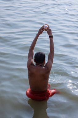Varanasi, Uttar Pradesh, Hindistan - Kasım 2022: Tanımlanamayan Brahmin erkek, gündoğumu sırasında Hindu ayinlerini gerçekleştirmek için nehir çetelerine kutsal dalışı yapıyor..
