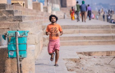 Varanasi, Uttar Pradesh, Hindistan - Kasım 2022: Varanasi şehrindeki nehir çetelerinin yakınlarındaki ghatlarda güneşlenen kimliği belirsiz Hintli erkek portresi.