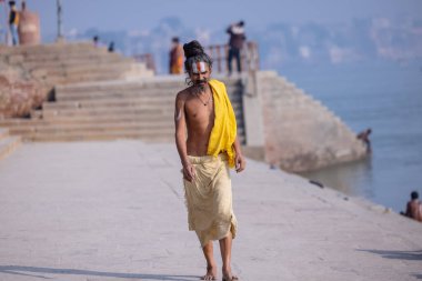 Varanasi, Uttar Pradesh, Hindistan - Kasım 2022: Geleneksel elbise içinde Varanasi şehrinde nehir çetelerinin yanındaki ghat üzerinde yürüyen tanımlanamayan Hint sadhu baba portresi. Varanasi en eski ve kutsal şehirdir..