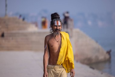 Varanasi, Uttar Pradesh, Hindistan - Kasım 2022: Geleneksel elbise içinde Varanasi şehrinde nehir çetelerinin yanındaki ghat üzerinde yürüyen tanımlanamayan Hint sadhu baba portresi. Varanasi en eski ve kutsal şehirdir..
