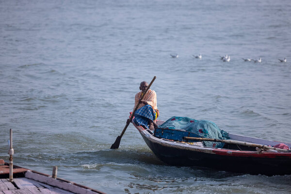 Varanasi, Uttar Pradesh, India - November 2022: Tourists enjoying boat ride in the river ganges along with the herd of sea gulls at varanasi during early morning. Boatman sailing the wooden boat.