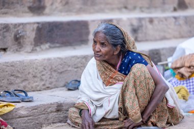 Varanasi, Uttar Pradesh, Hindistan - Kasım 2022: Geleneksel saride çetelerin yanında oturan yaşlı bir Hintli kadının portresi.