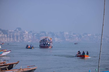 Varanasi, Uttar Pradesh, Hindistan - Kasım 2022: Turistler sabah erken saatlerde Varanasi 'deki martı sürüsüyle birlikte nehir çetelerinde tekne gezintisi yapıyorlar. Tahta teknede yelken açan kayıkçı.