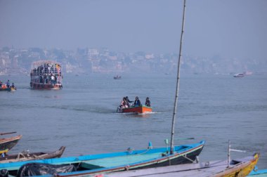 Varanasi, Uttar Pradesh, Hindistan - Kasım 2022: Turistler sabah erken saatlerde Varanasi 'deki martı sürüsüyle birlikte nehir çetelerinde tekne gezintisi yapıyorlar. Tahta teknede yelken açan kayıkçı.