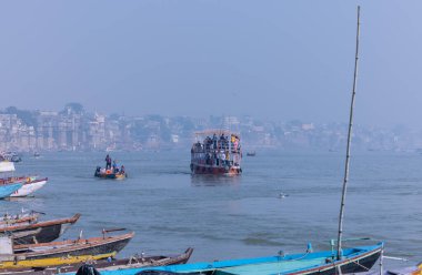 Varanasi, Uttar Pradesh, Hindistan - Kasım 2022: Turistler sabah erken saatlerde Varanasi 'deki martı sürüsüyle birlikte nehir çetelerinde tekne gezintisi yapıyorlar. Tahta teknede yelken açan kayıkçı.