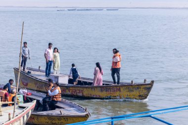 Varanasi, Uttar Pradesh, Hindistan - Kasım 2022: Turistler sabah erken saatlerde Varanasi 'deki martı sürüsüyle birlikte nehir çetelerinde tekne gezintisi yapıyorlar. Tahta teknede yelken açan kayıkçı.
