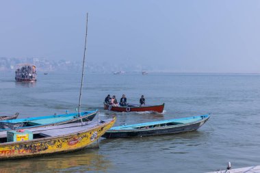 Varanasi, Uttar Pradesh, Hindistan - Kasım 2022: Turistler sabah erken saatlerde Varanasi 'deki martı sürüsüyle birlikte nehir çetelerinde tekne gezintisi yapıyorlar. Tahta teknede yelken açan kayıkçı.