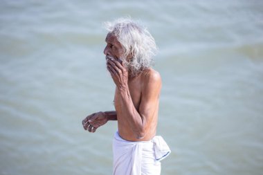 Varanasi, Uttar Pradesh, Hindistan - Kasım 2022: Kimliği belirsiz erkek portresi, gündoğumu sırasında Hint ritüeli olarak kutsal dalış yapmak için nehir çetelerinin yanında duruyordu.